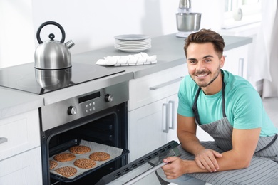 Young man baking cookies in oven at home