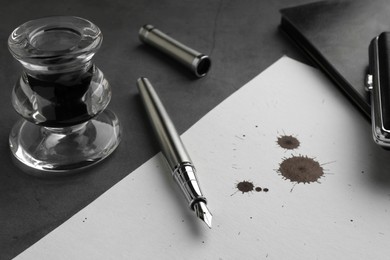 Stylish fountain pen, paper with blots of ink and inkwell on grey textured table