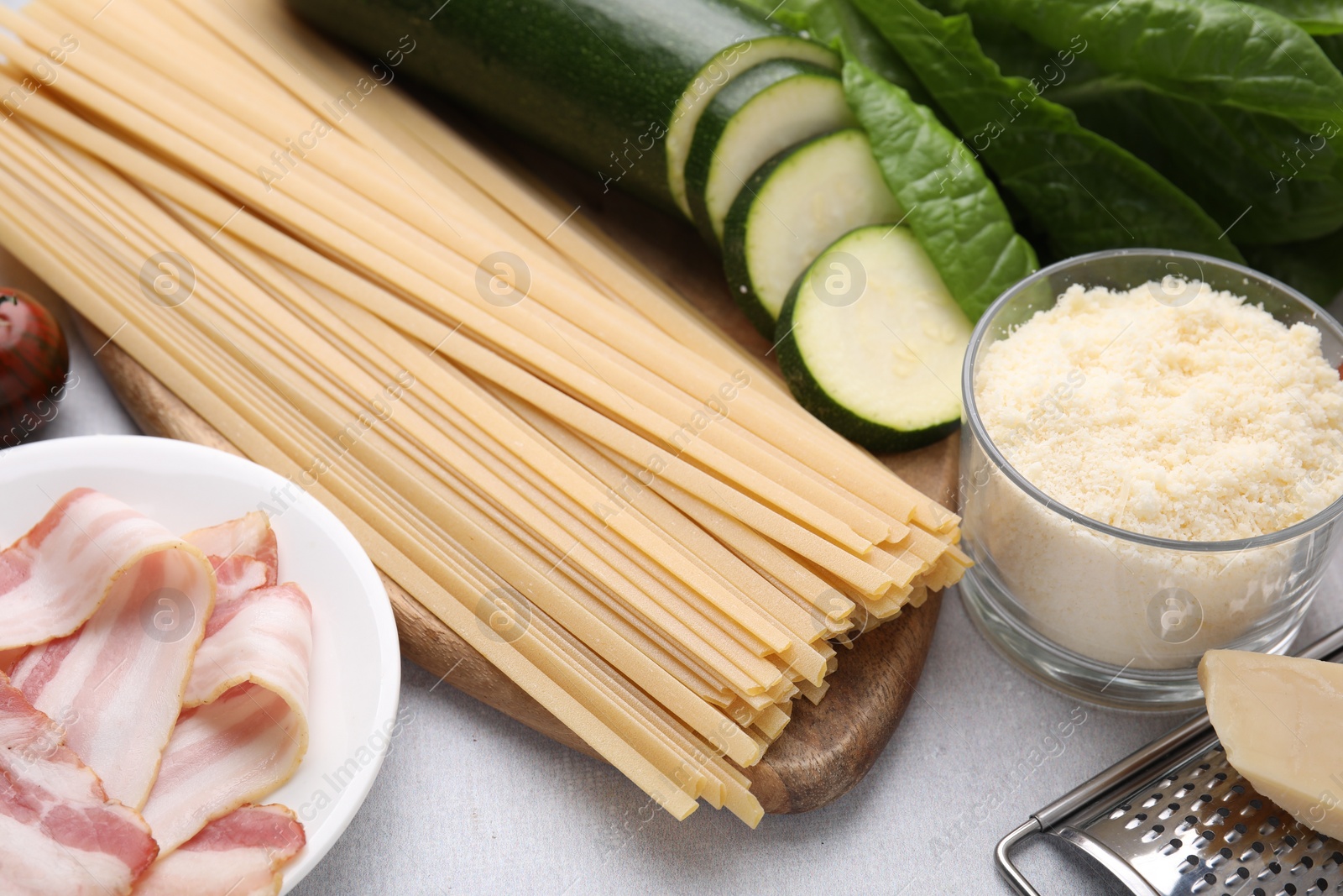 Photo of Raw pasta, bacon and fresh ingredients on light grey table