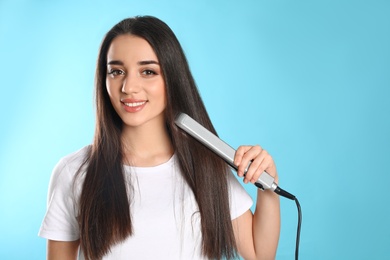 Happy woman using hair iron on color background. Space for text