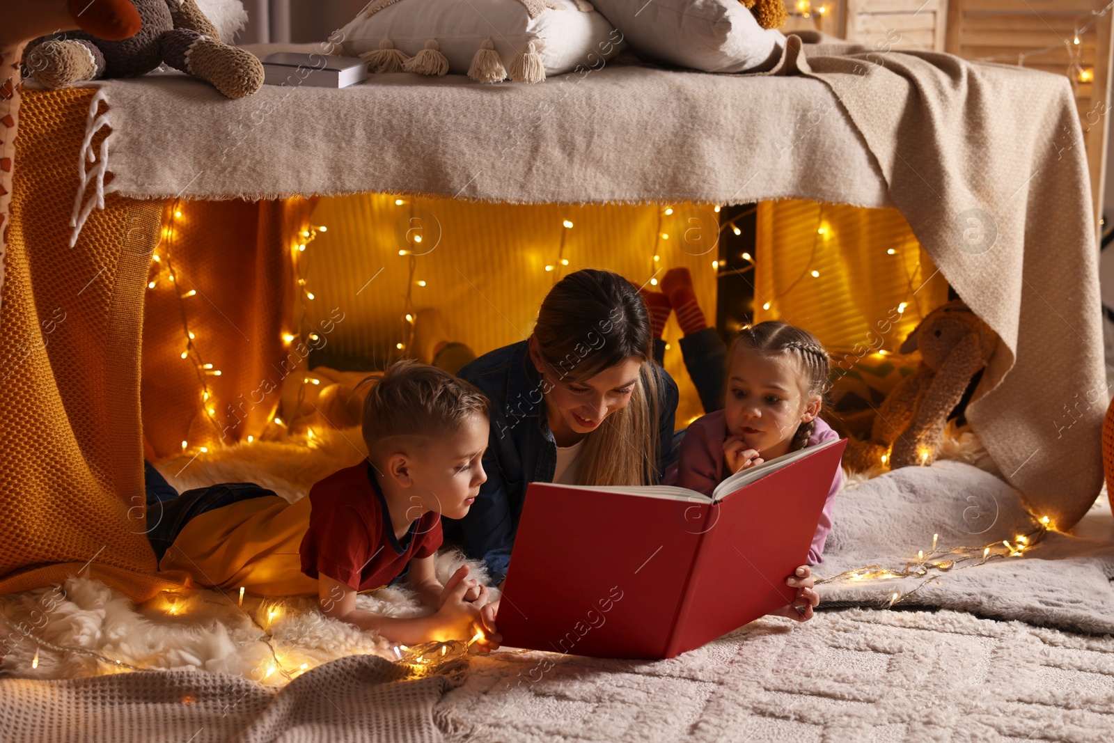 Photo of Mother and her children reading book in play tent at home