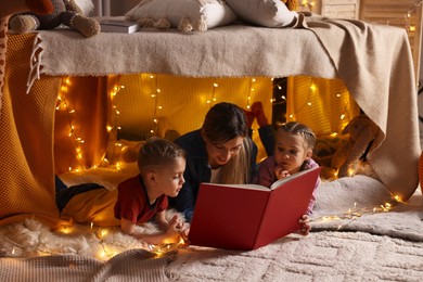 Mother and her children reading book in play tent at home