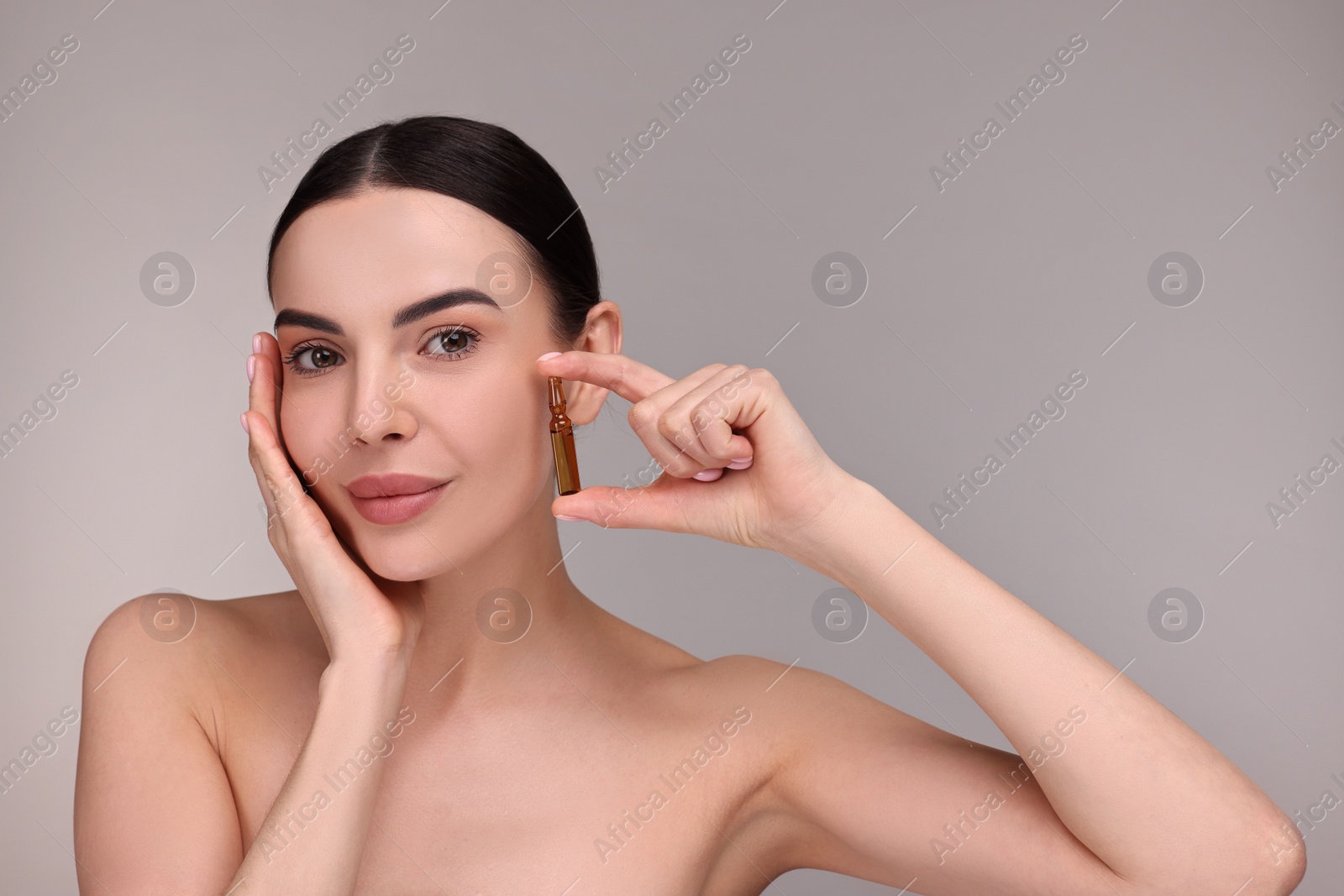 Photo of Beautiful young woman holding skincare ampoule on grey background. Space for text