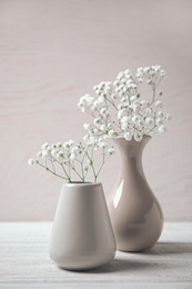 Photo of Gypsophila flowers in vases on table against light background