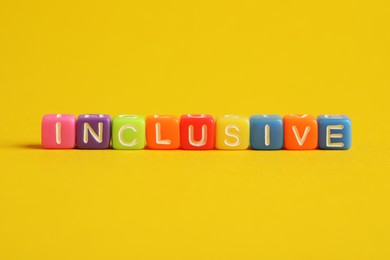 Photo of Colorful cubes with word Inclusive on yellow background