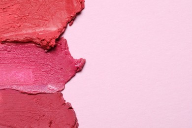Photo of Smears of beautiful lipsticks on pink background, top view. Space for text