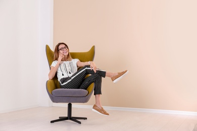 Photo of Young woman talking on phone in armchair at home. Space for text