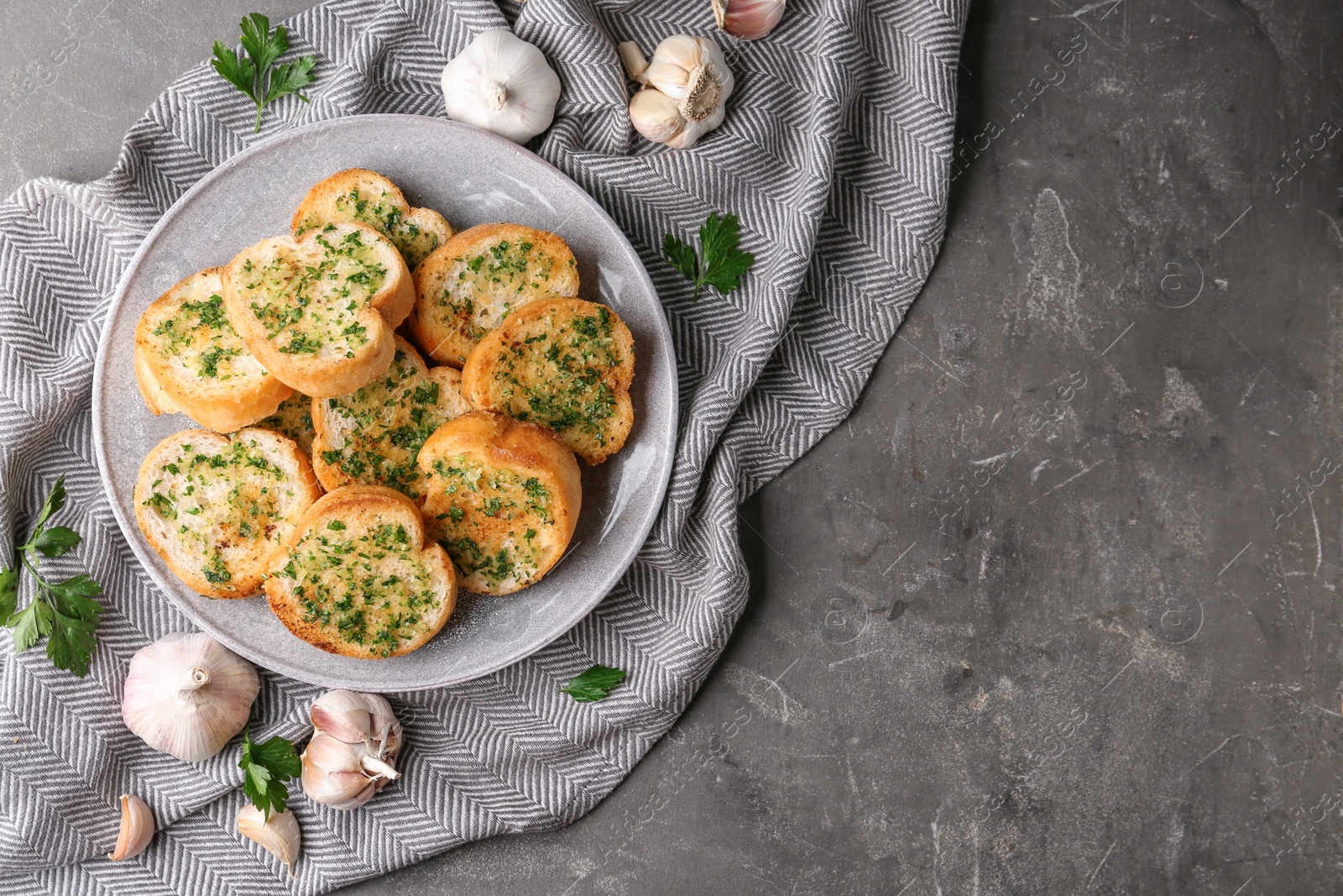 Photo of Slices of toasted bread with garlic and herbs on grey table, flat lay. Space for text