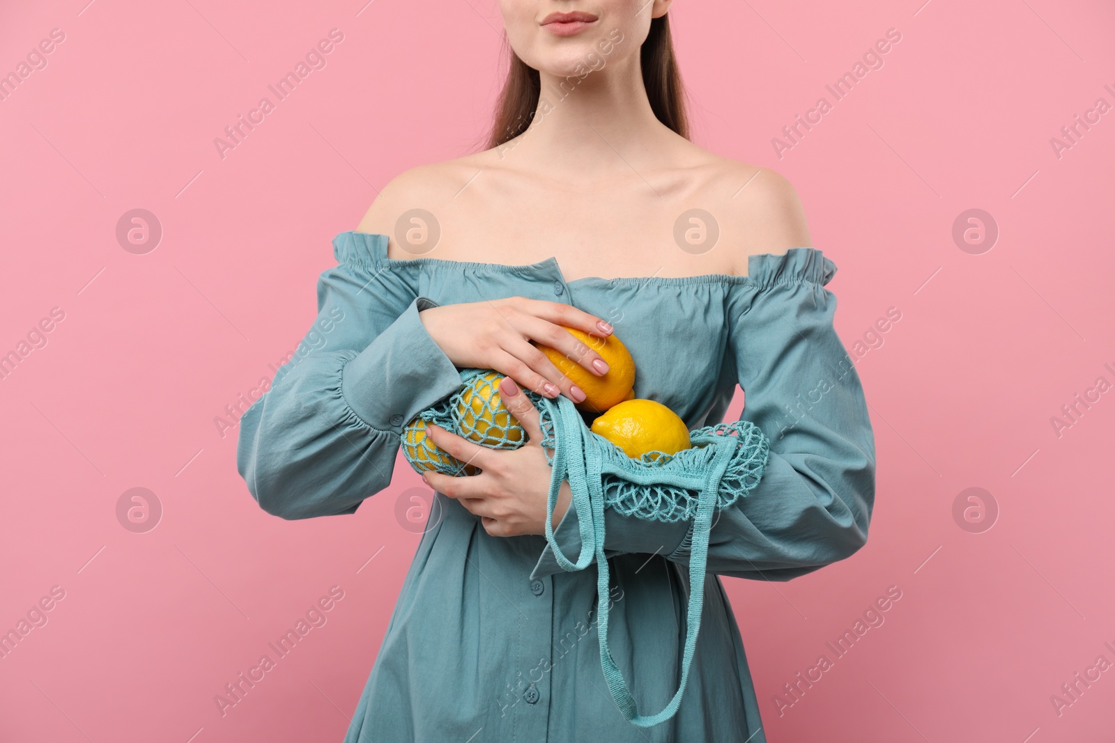 Photo of Woman with string bag of fresh lemons on pink background, closeup