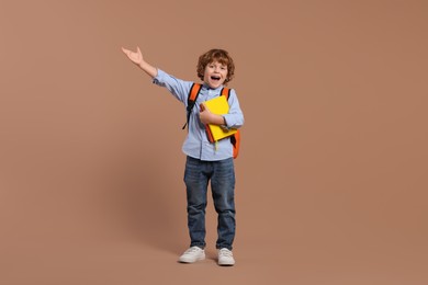 Photo of Emotional schoolboy with backpack and books on brown background