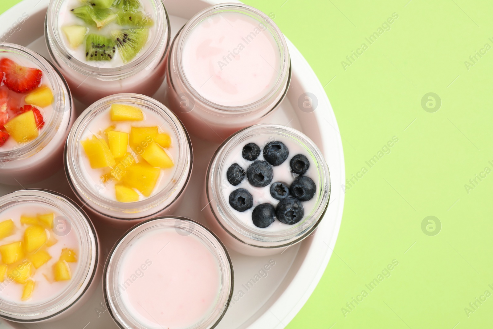 Photo of Yogurt maker with jars and different fruits on light green background, top view. Space for text