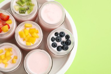 Photo of Yogurt maker with jars and different fruits on light green background, top view. Space for text