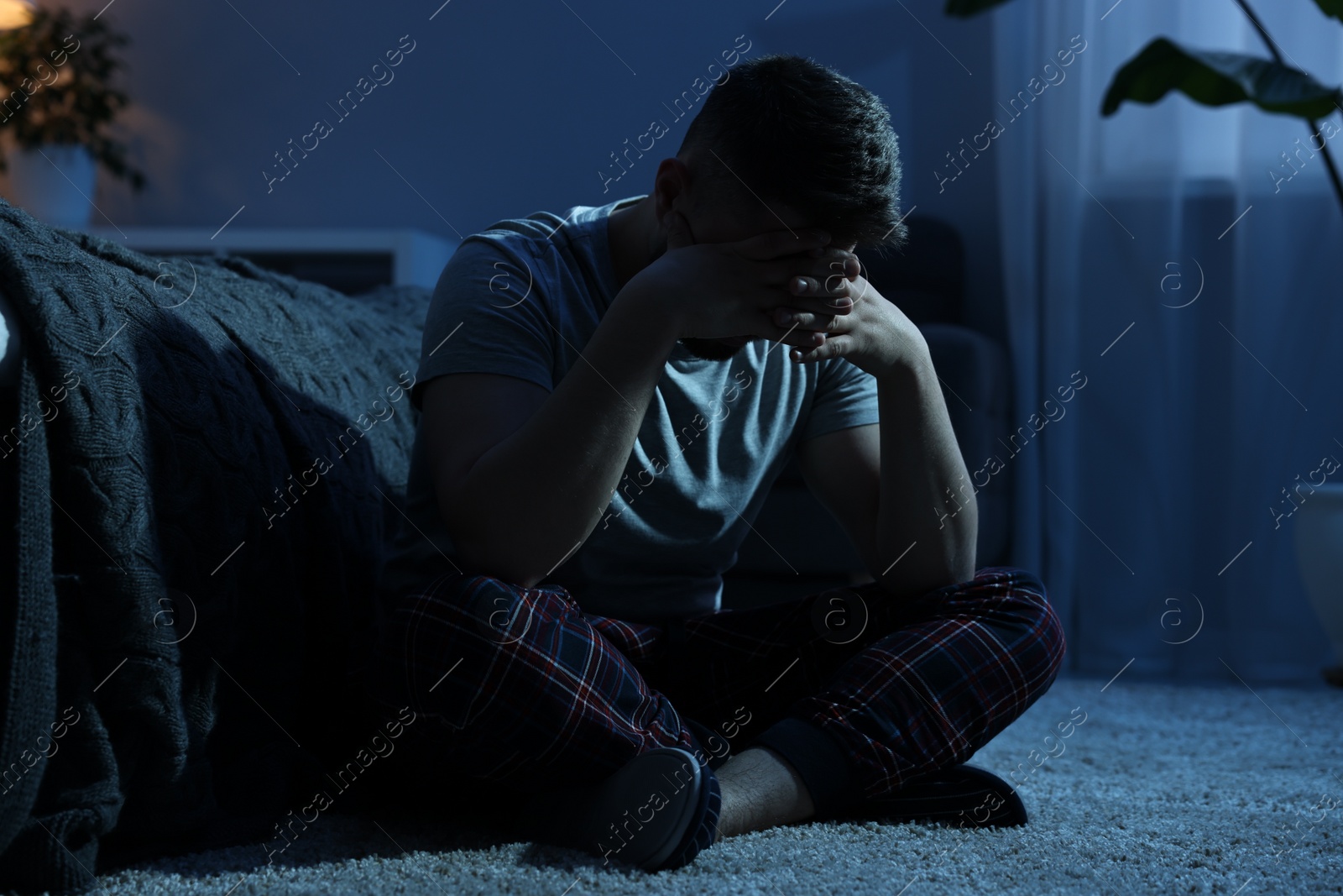 Photo of Man covering face with hands on carpet at night