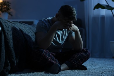 Man covering face with hands on carpet at night