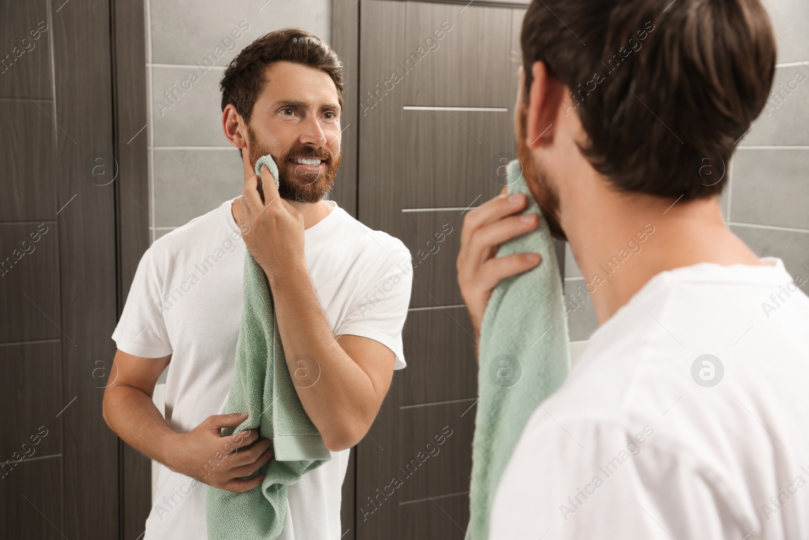Photo of Handsome man drying his beard in front of mirror in bathroom