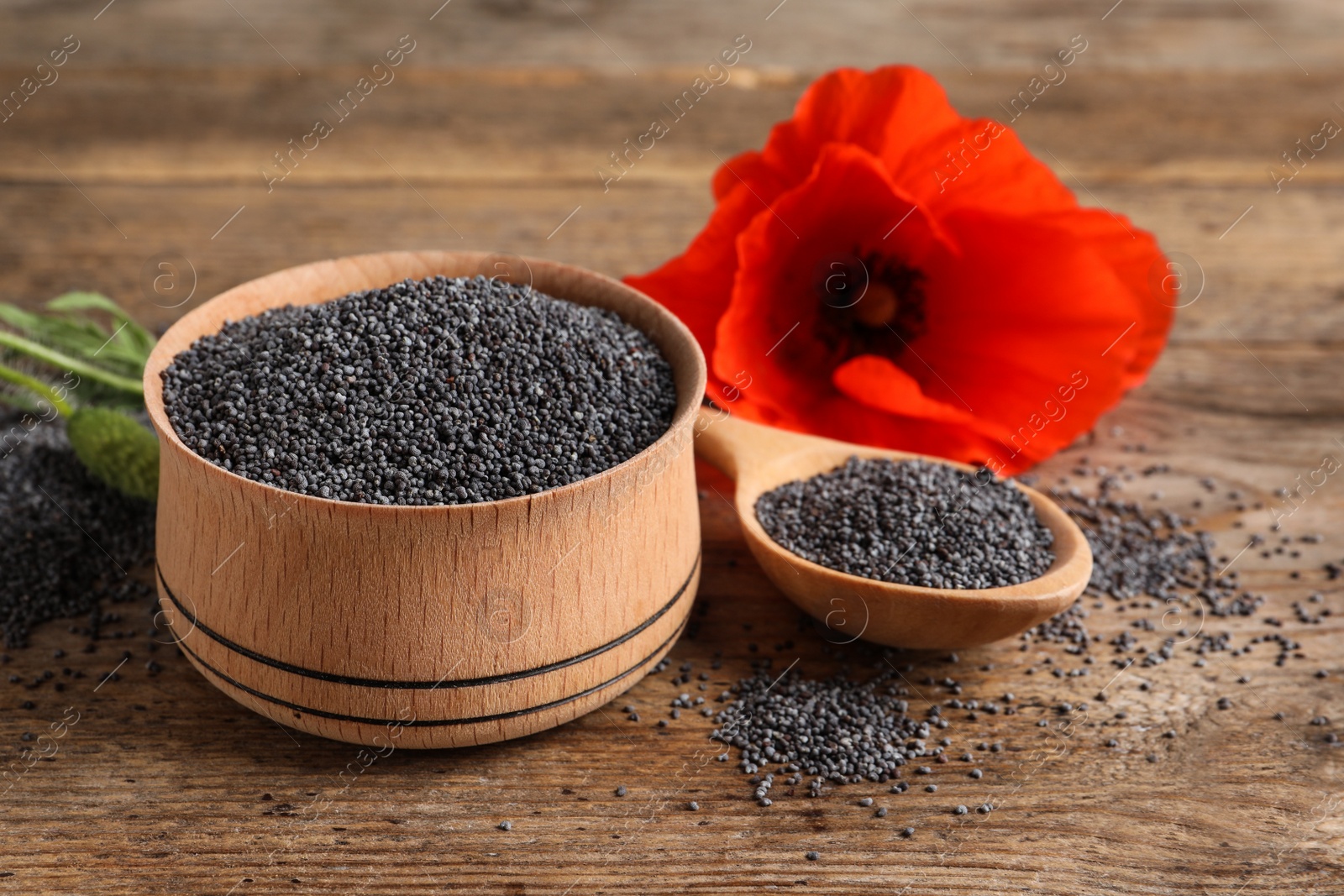 Photo of Wooden bowl of poppy seeds, spoon and flower on table, space for text