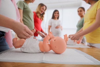 Photo of Pregnant women learning how to swaddle baby at courses for expectant mothers indoors, closeup
