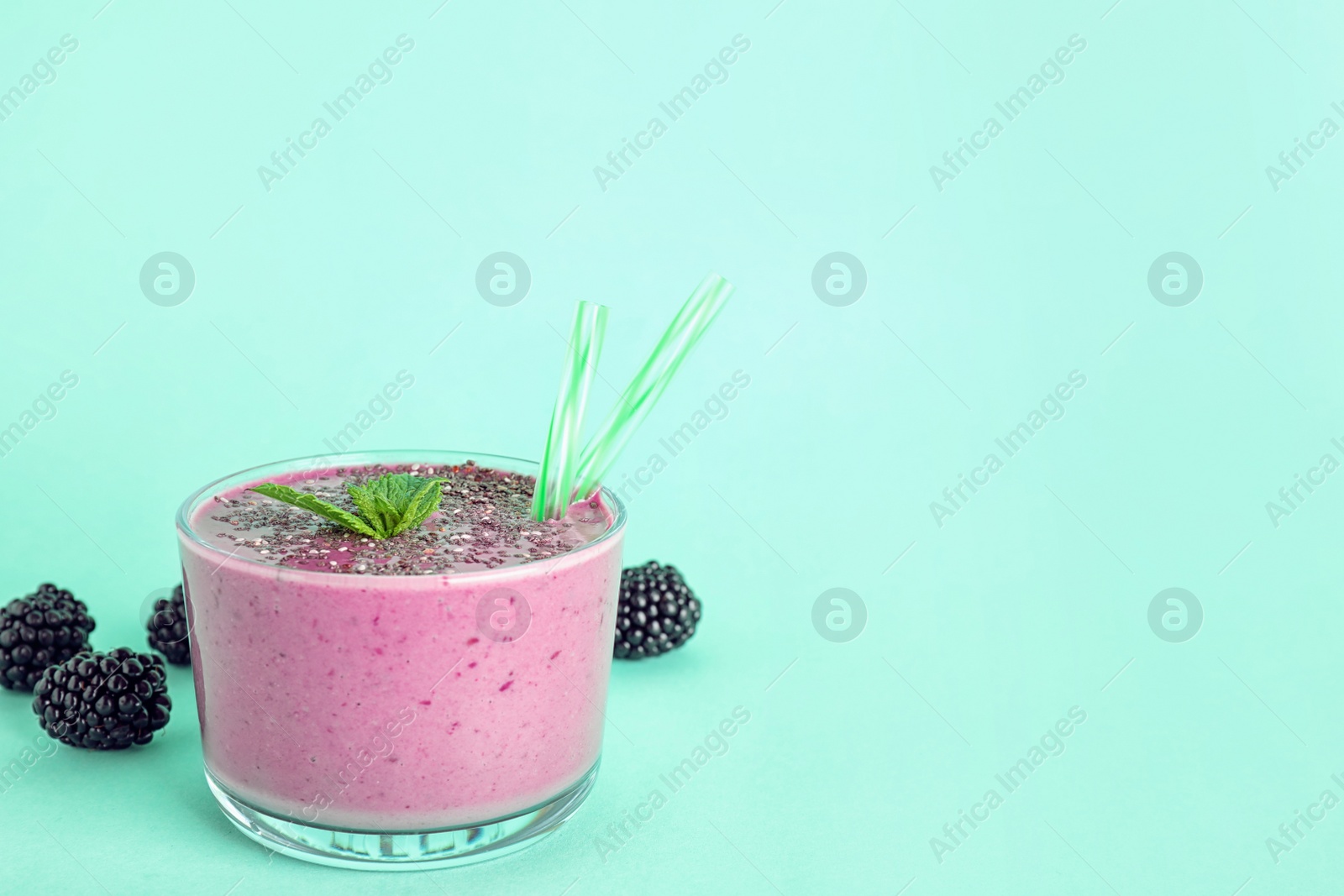 Photo of Glass of tasty blackberry smoothie with chia seeds and straws on turquoise background. Space for text