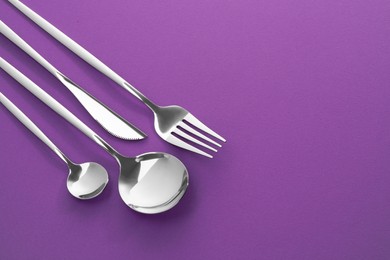 Fork, knife and spoons on purple background, flat lay with space for text. Stylish cutlery set