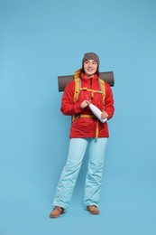 Smiling young woman with backpack and thermo bottle on light blue background. Active tourism