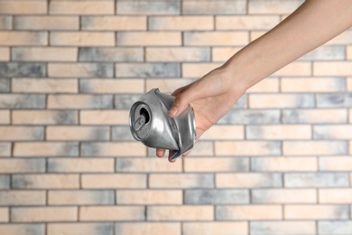 Photo of Woman holding crumpled aluminum can on brick wall background. Metal waste recycling