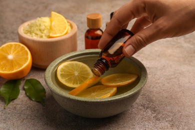 Photo of Woman dripping essential oil into bowl with lemons at grey textured table, closeup. Aromatherapy treatment