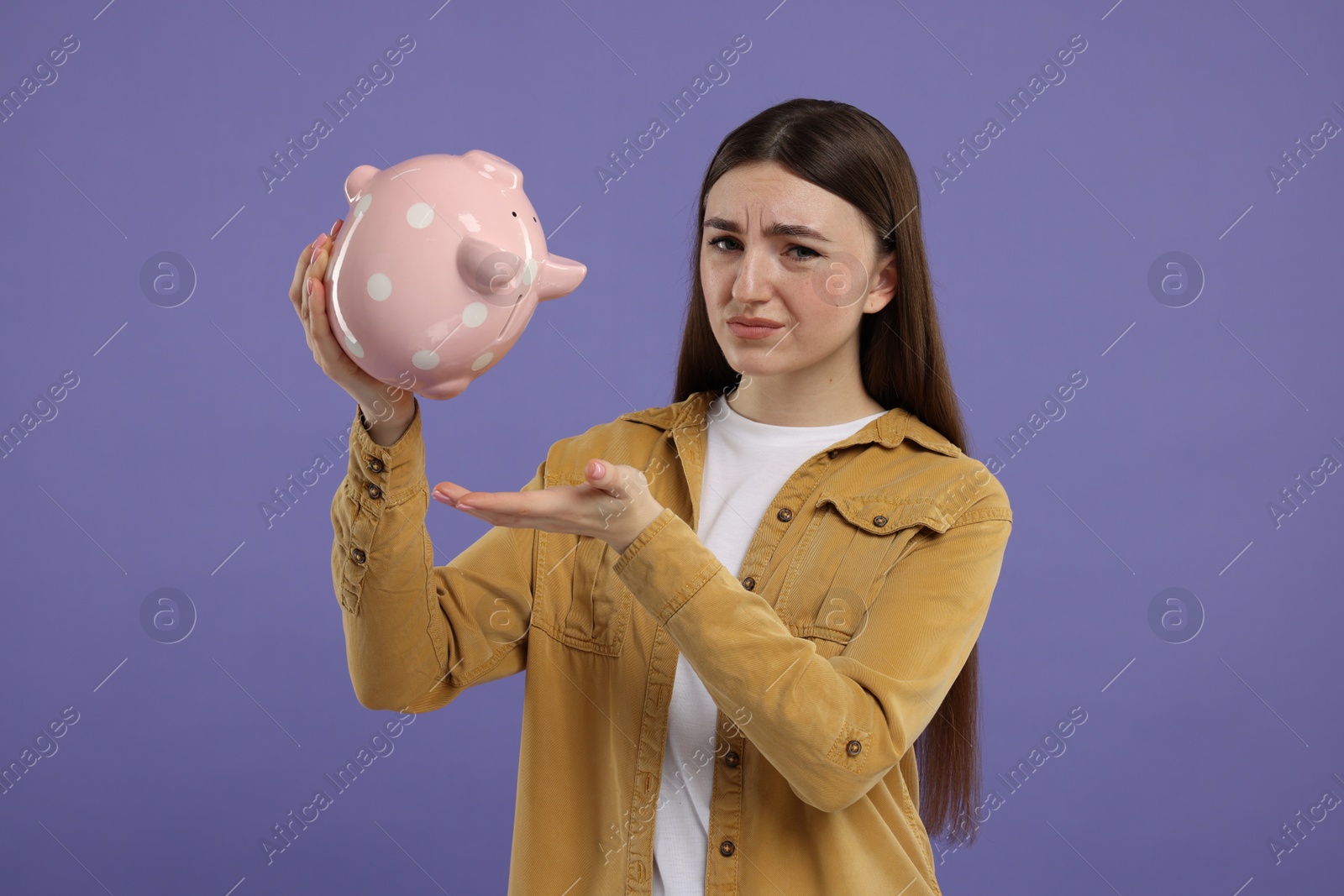 Photo of Sad woman with piggy bank on purple background