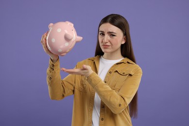 Sad woman with piggy bank on purple background