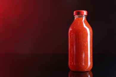 Photo of Spicy chili sauce in bottle against dark background, space for text