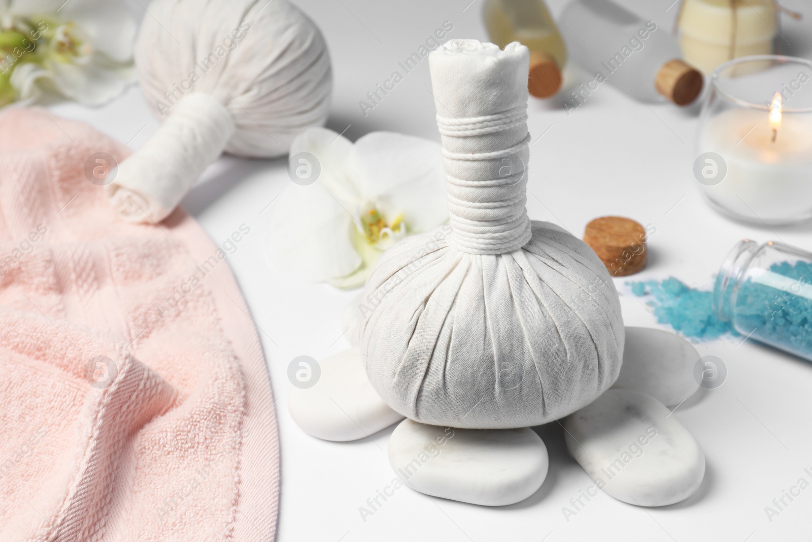 Photo of Herbal massage bags, spa stones, sea salt and towel on white table