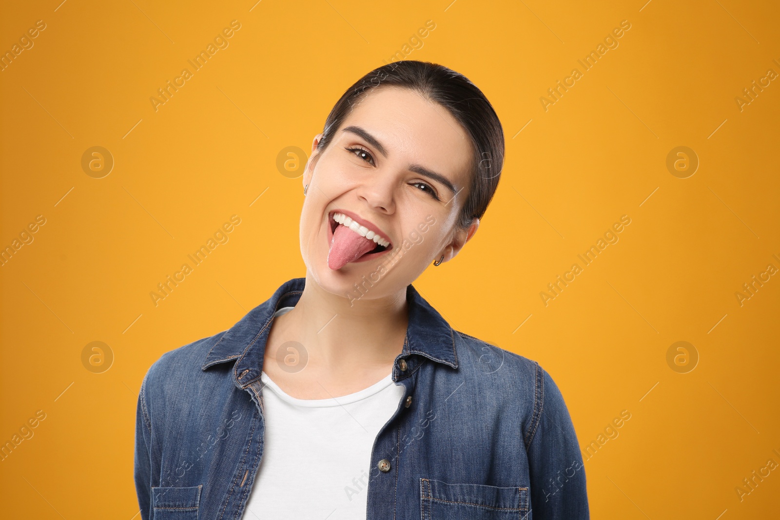 Photo of Happy young woman showing her tongue on yellow background