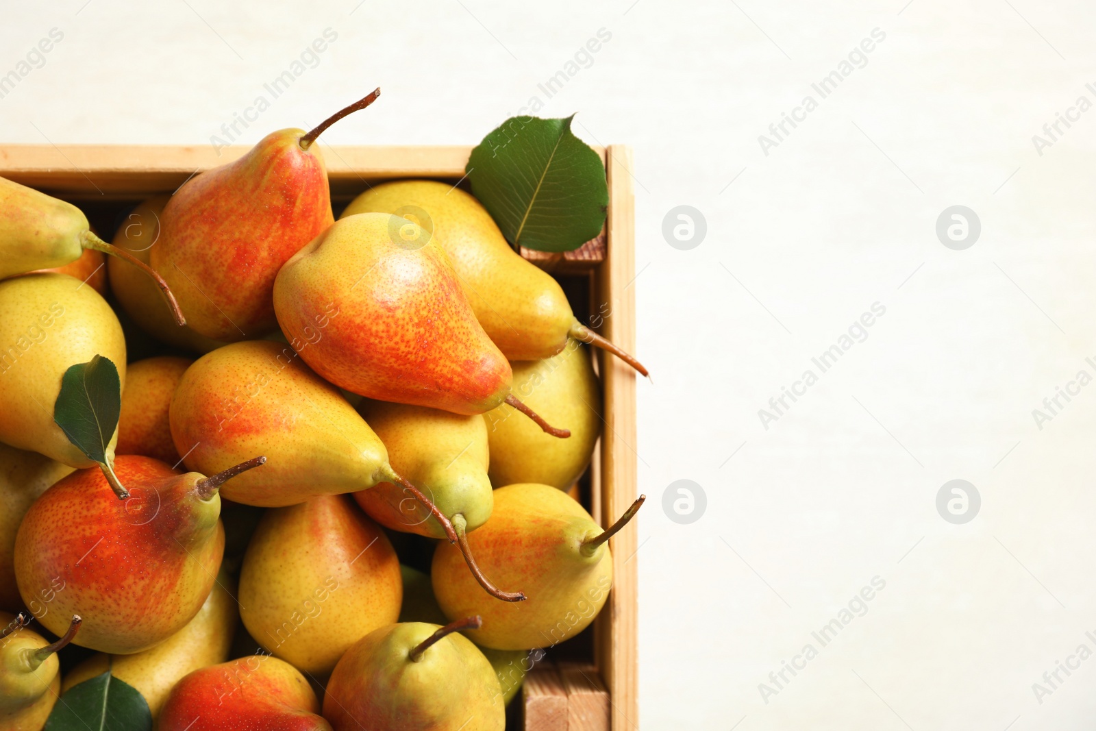 Photo of Wooden crate with ripe pears on light background, top view. Space for text