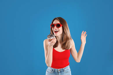 Beautiful young woman wearing sunglasses with donut on blue background
