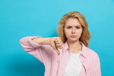 Photo of Dissatisfied young woman showing thumb down gesture on light blue background