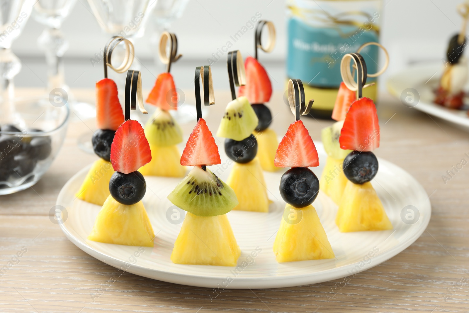 Photo of Tasty canapes with pineapple, kiwi and berries on light wooden table, closeup