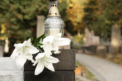 Photo of White lilies and grave light on grey granite tombstone outdoors, space for text. Funeral ceremony