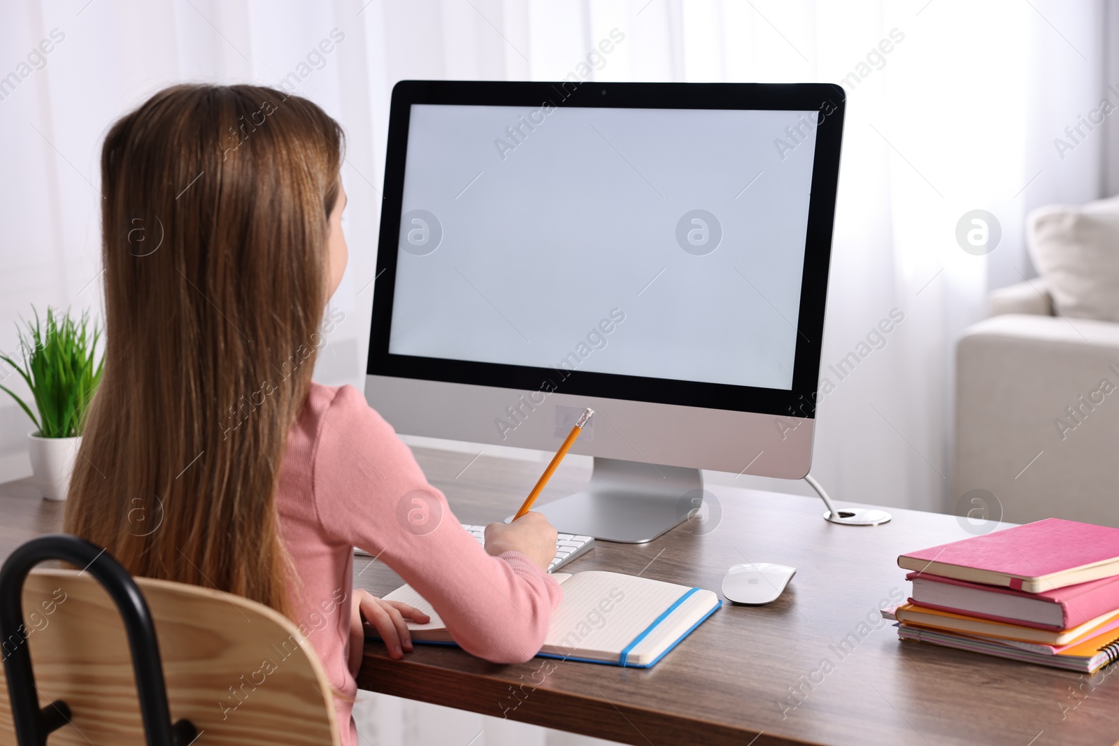 Photo of E-learning. Cute girl taking notes during online lesson at table indoors