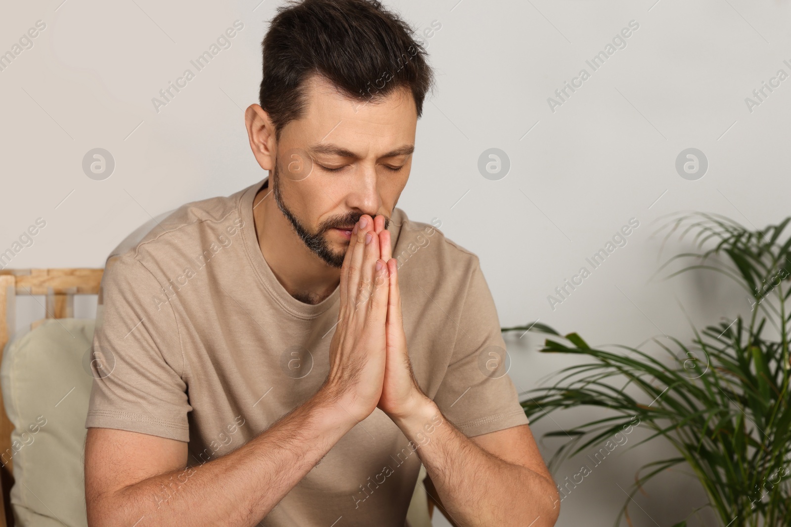 Photo of Man with clasped hands praying in room at home