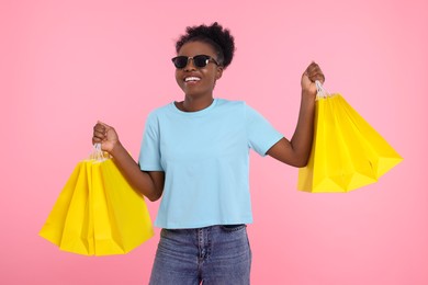 Photo of Happy young woman in stylish sunglasses with shopping bags on pink background