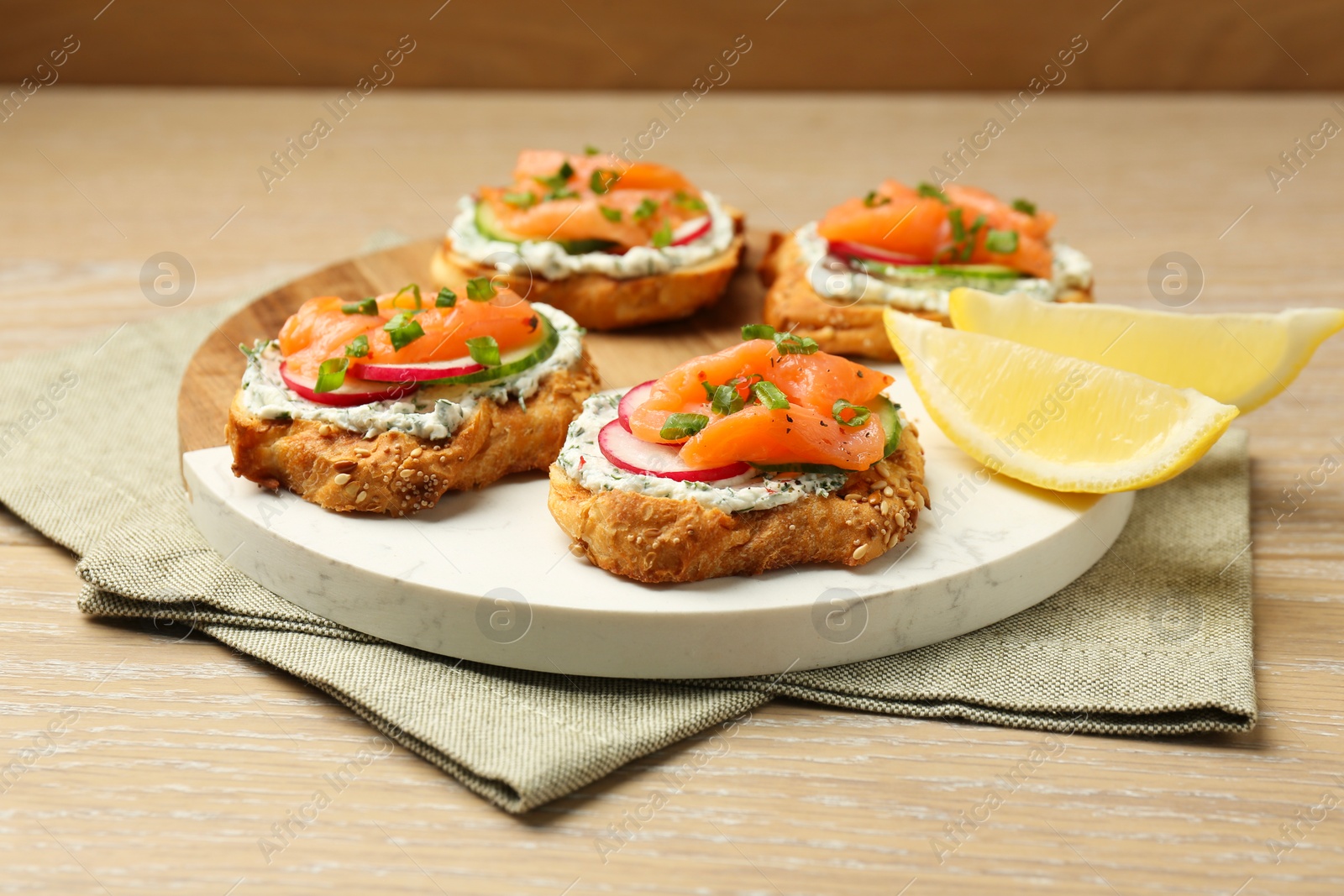 Photo of Tasty canapes with salmon, cucumber, radish and cream cheese on wooden table