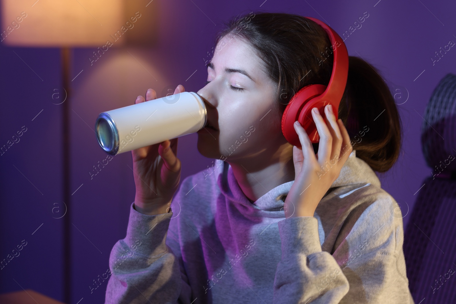 Photo of Girl in headphones with can of energy drink at home