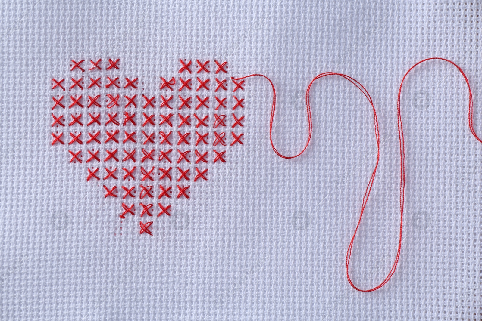 Photo of Embroidered red heart on white cloth, top view