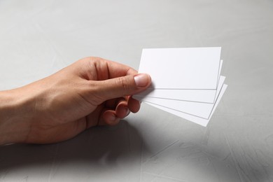 Man holding white blank cards at light grey table, closeup. Mockup for design