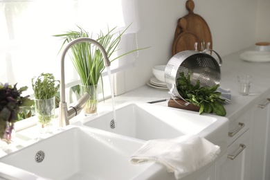 Colander with fresh spinach on countertop near sink in kitchen