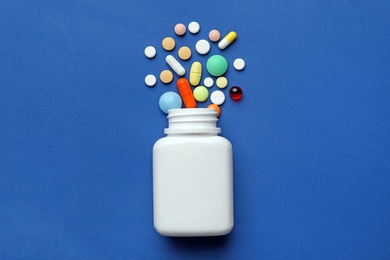 Bottle with different pills on color background, flat lay