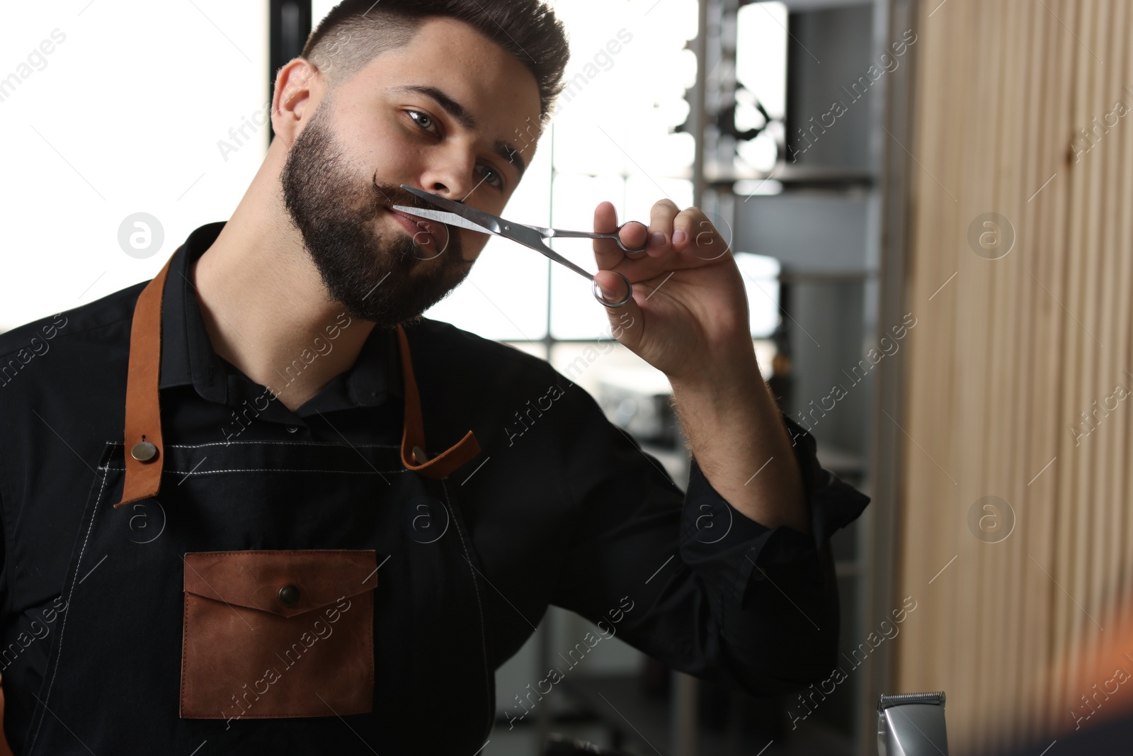 Photo of Handsome young man trimming mustache with scissors near mirror indoors