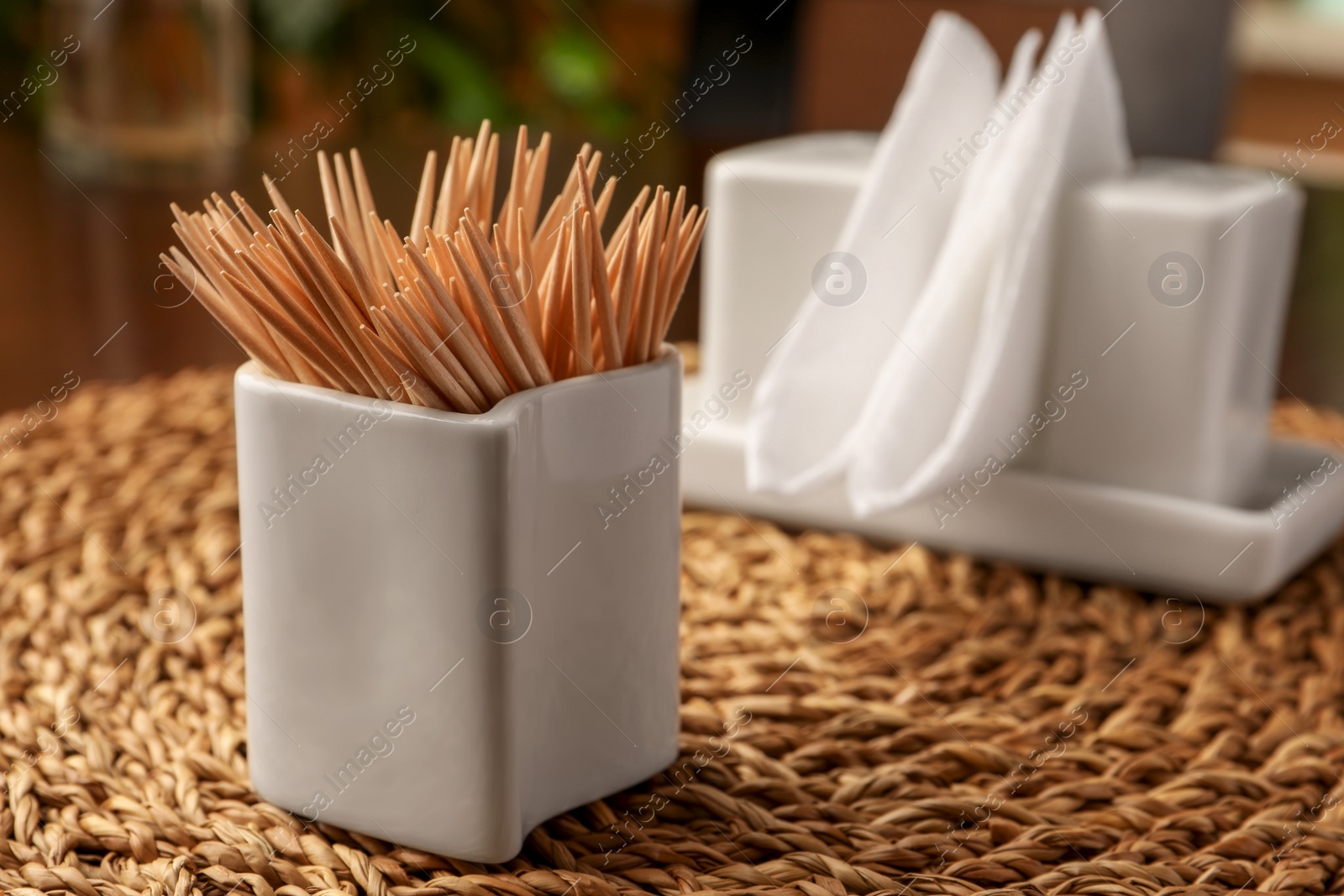 Photo of Wooden holder with many toothpicks on wicker mat, closeup. Space for text