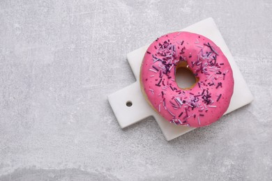 Photo of Sweet glazed donut decorated with sprinkles on light grey table, top view and space for text. Tasty confectionery