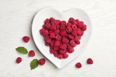 Photo of Plate with ripe aromatic raspberries on table, top view