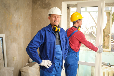 Workers in uniform installing plastic window indoors